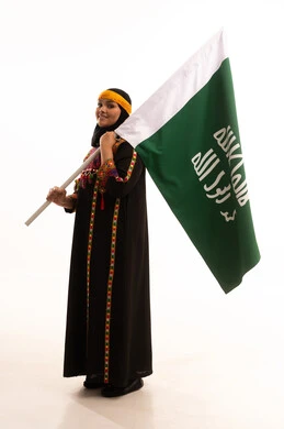 الاحتفال بالمناسبات والأعياد الوطنية الشعبية، ذكرى تأسيس الدولة السعودية الأولى 22 فبراير، يوم بدينا 1727 م، ارتداء أزياء المنطقة الوسطى، بورتريه لإمرأة عربية خليجية سعودية مبتسمة ترتدي الكرتة والهامة تحمل بيدها علم يوم التأسيس، الجسم بالطول الكامل، خلفية بيضاء