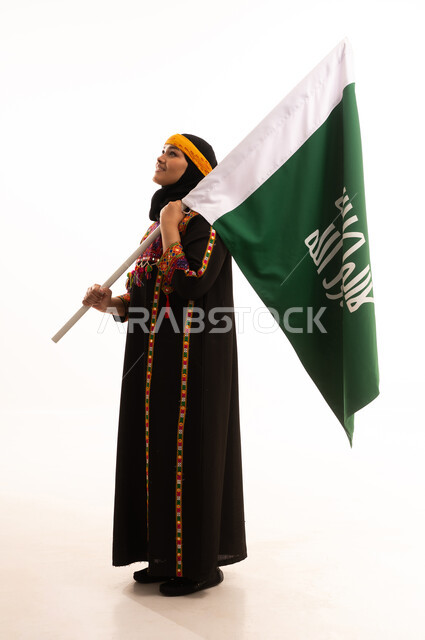 يوم بدينا 1727 م، الاحتفال بالمناسبات والأعياد الوطنية الشعبية، ذكرى تأسيس الدولة السعودية الأولى 22 فبراير، ارتداء أزياء المنطقة الوسطى، بورتريه لإمرأة عربية خليجية سعودية مبتسمة ترتدي الكرتة والهامة تحمل بيدها علم يوم التأسيس، الجسم بالطول الكامل، خلفية بيضاء