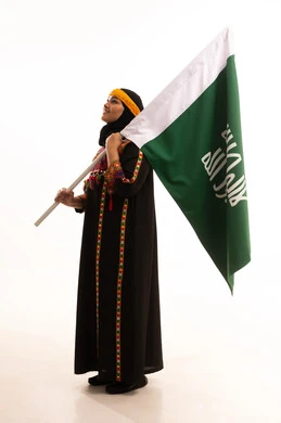 The Day We Began 1727 AD, celebrating national occasions and popular holidays, the anniversary of the founding of the first Saudi state, February 22, wearing the costumes of the central region, a portrait of a smiling Saudi Arabian Gulf woman wearing a kurta and a hat, holding the Founding Day flag in her hand, full-length body, white background