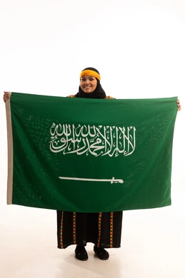 Pride in historical heritage, Flag Day March 11, the day we started in 1727 AD, wearing the Central Region costume, Saudi National Day September 23, portrait of a Saudi Arabian Gulf woman wearing a kurta and a head holding the Kingdom's flag looking at the camera with an expression of pride, full body, white background