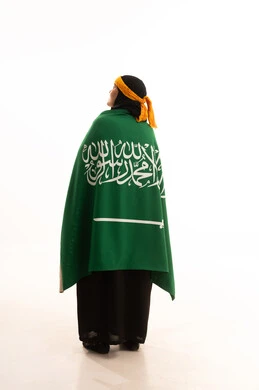 مفهوم حب الوطن، اليوم الوطني السعودي 23 سبتمبر, يوم بدينا 1727م, الفخر بالتراث التاريخي، يوم العلم 11 مارس، ارتداء زي المنطقة الوسطى، بورتريه من الخلف لإمرأة عربية خليجية سعودية ترتدي الكرتة والهامة تحمل علم المملكة, الجسم بالطول الكامل، خلفية بيضاء