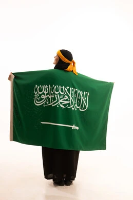 The concept of patriotism, Saudi National Day September 23, the day we started in 1727 AD, pride in historical heritage, Flag Day March 11, wearing the Central Region costume, a portrait from the back of a Saudi Arabian Gulf woman wearing a kurta and a head holding the flag of the Kingdom, full body, white background