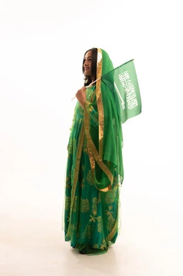 Saudi National Day, September 23, raising the banner of monotheism and Islam, Flag Day, March 11, wearing the traditional costume of the central region on a national occasion, Badina Day, February 22, side portrait of a Saudi Arabian Gulf woman wearing a shayla and bisht holding the flag of the Kingdom, full body length, white background