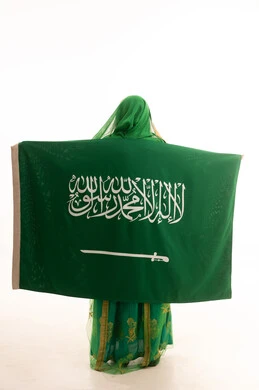 الحب والولاء للوطن، اليوم الوطني السعودي 23 سبتمبر، يوم العلم 11 مارس، ارتداء الزي الشعبي للمنطقة الوسطى , يوم بدينا22 فبراير, بورتريه من الخلف لامرأة عربية خليجية سعودية ترتدي الشيلة والبشت تضع على كتفيها علم المملكة، الطول الكامل للجسم، خلفية بيضاء