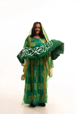 ارتداء الزي الشعبي للمنطقة الوسطى في مناسبة وطنية, النظر إلى الكاميرا بإيماءات الاعتزاز، يوم العلم 11 مارس، يوم بدينا22 فبراير, اليوم الوطني السعودي 23 سبتمبر، بورتريه لامرأة عربية خليجية سعودية ترتدي الشيلة والبشت تمسك علم المملكة، الطول الكامل للجسم، خلفية بيضاء