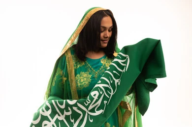 الاعتزاز والفخر بالانتماء للوطن، اليوم الوطني السعودي 23 سبتمبر، يوم العلم 11 مارس، ارتداء الزي الشعبي للمنطقة الوسطى في مناسبة وطنية, يوم بدينا22 فبراير, بورتريه مقرب لامرأة عربية خليجية سعودية ترتدي الشيلة والبشت تحمل علم المملكة، خلفية بيضاء