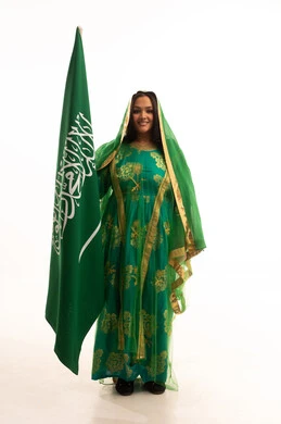 Looking at the camera with gestures of pride, Flag Day March 11, Badina Day February 22, wearing the traditional costume of the central region on a national occasion, Saudi National Day September 23, portrait of a Saudi Arabian Gulf woman wearing a sheila and bisht holding the flag of the Kingdom, full body length, white background