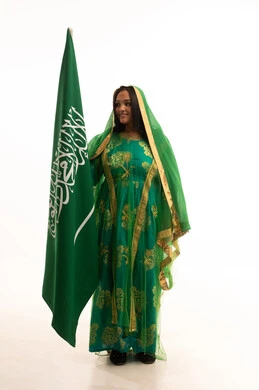الوقوف باستقامة بإيماءات الشموخ، ارتداء الزي الشعبي للمنطقة الوسطى في مناسبة وطنية, يوم العلم 11 مارس، يوم بدينا22 فبراير, اليوم الوطني السعودي 23 سبتمبر، بورتريه لامرأة عربية خليجية سعودية ترتدي الشيلة والبشت تمسك علم المملكة، الطول الكامل للجسم، خلفية بيضاء