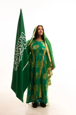 رفع راية التوحيد والإسلام، يوم العلم 11 مارس، ارتداء الزي الشعبي للمنطقة الوسطى في مناسبة وطنية, يوم بدينا22 فبراير, اليوم الوطني السعودي 23 سبتمبر، بورتريه لامرأة عربية خليجية سعودية ترتدي الشيلة والبشت تمسك علم المملكة، الطول الكامل للجسم، خلفية بيضاء