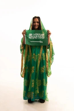 ارتداء الزي الشعبي للمنطقة الوسطى في مناسبة وطنية, النظر إلى الكاميرا بإيماءات الاعتزاز، يوم العلم 11 مارس، يوم بدينا22 فبراير, اليوم الوطني السعودي 23 سبتمبر، بورتريه لامرأة عربية خليجية سعودية ترتدي الشيلة والبشت تمسك علم المملكة، الطول الكامل للجسم، خلفية بيضاء