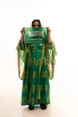 Looking at the camera with gestures of pride, Flag Day March 11, Badina Day February 22, wearing the traditional costume of the central region on a national occasion, Saudi National Day September 23, portrait of a Saudi Arabian Gulf woman wearing a sheila and bisht holding the flag of the Kingdom, full body length, white background