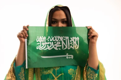 Pride and honor of belonging to the homeland, Saudi National Day September 23, Flag Day March 11, wearing the traditional costume of the central region on a national occasion, Badina Day February 22, close-up portrait of a Saudi Arabian Gulf woman wearing a shayla and bisht holding the flag of the Kingdom, white background