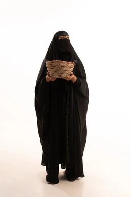 Traditional folk professions and crafts, celebrating Badina Day 1727 AD, women's handicrafts, the anniversary of the founding of the first Saudi state, February 22, portrait of a Saudi Arabian Gulf woman wearing a burqa and black abaya carrying a basket made of straw, full body image, white background
