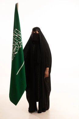 Pride and pride in belonging to the country, our beginning day, February 22, Saudi National Day, September 23, wearing traditional dress on a national occasion, Flag Day, March 11, portrait of a Saudi Arabian Gulf woman wearing a burqa and abaya holding the flag of the Kingdom, full body length, white background
