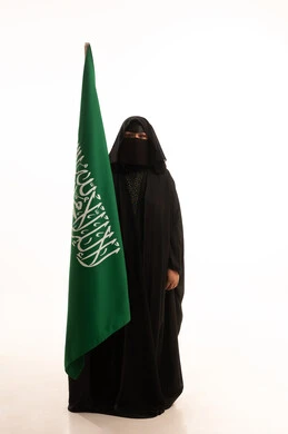 رفع راية التوحيد والإسلام، يوم العلم 11 مارس، يوم بدينا22 فبراير, ارتداء الزي الشعبي في مناسبة وطنية, الاحتفال بذكرى اليوم الوطني السعودي 23 سبتمبر، بورتريه لامرأة عربية خليجية سعودية ترتدي البرقع والعباءة تمسك علم المملكة، الطول الكامل للجسم، خلفية بيضاء