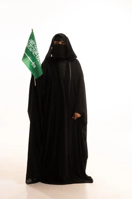 Raising the flag of unity and Islam, Flag Day March 11, Badina Day February 22, wearing traditional dress on a national occasion, celebrating Saudi National Day September 23, portrait of a Saudi Arabian Gulf woman wearing a burqa and abaya holding the flag of the Kingdom, full body length, white background