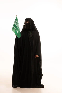 The concept of love of the homeland and belonging to it, the day we started February 22, Saudi National Day September 23, wearing traditional dress on a national occasion, Flag Day March 11, portrait of a Saudi Arabian Gulf woman wearing a burqa and abaya holding the flag of the Kingdom, full body length, white background