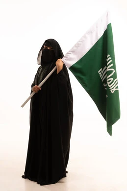 الفخر بإنجازات المملكة، إظهار الولاء والحب للوطن, ذكرى تأسيس الدولة السعودية الأولى 1727م، بورتريه لامرأة عربية خليجية سعودية ترتدي البرقع والعباءة تحمل علم التأسيس تنظر إلى الكاميرا بإيماءات الاعتزاز والشموخ، يوم بدينا 22 فبراير، الجسم بالطول الكامل، خلفية بيضاء