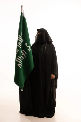 Anniversary of the founding of the first Saudi state 1727 AD, pride in the achievements of the Kingdom, showing loyalty and love for the homeland, portrait of a Saudi Arabian Gulf woman wearing a burqa and abaya holding the founding flag with gestures of pride and loftiness, the day we began, February 22, full-length body, white background