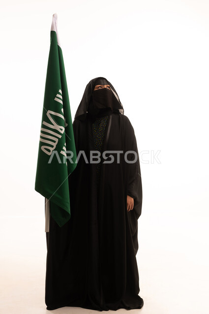 ذكرى تأسيس الدولة السعودية الأولى 1727م، الفخر بإنجازات المملكة، إظهار الولاء والحب للوطن, بورتريه لامرأة عربية خليجية سعودية ترتدي البرقع والعباءة تحمل علم التأسيس بإيماءات الاعتزاز والشموخ، يوم بدينا 22 فبراير، الجسم بالطول الكامل، خلفية بيضاء