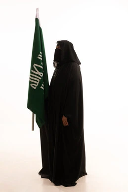 يوم بدينا 22 فبراير، ذكرى تأسيس الدولة السعودية الأولى 1727م، الفخر بإنجازات المملكة، إظهار الولاء والحب للوطن, بورتريه من الجانب لامرأة عربية خليجية سعودية ترتدي البرقع والعباءة تحمل علم التأسيس بإيماءات الاعتزاز والشموخ، الجسم بالطول الكامل، خلفية بيضاء