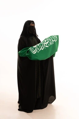 Looking up with expressions of pride and dignity, Saudi National Day September 23, wearing traditional dress on a national occasion, Flag Day March 11, Badina Day February 22, portrait of a Saudi Arabian Gulf woman wearing a burqa and abaya holding the flag of the Kingdom, full body length, white background