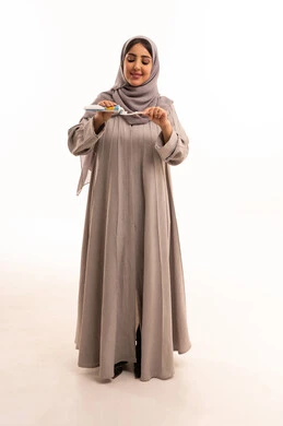 Using a toothbrush and toothpaste, the concept of healthy habits, maintaining and continuously cleaning teeth, a bright white smile, daily oral hygiene routine, avoiding cavities and gum diseases, a portrait of a Saudi Arabian Gulf woman wearing a hijab and abaya brushing her teeth, full body, white background.