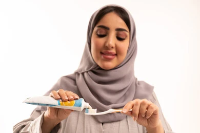 تجنب التسوس وأمراض اللثة، استخدام الفرشاة والمعجون، مفهوم العادات الصحية، الحفاظ على الأسنان وتنظيفها بشكل مستمر, ابتسامة ناصعة البياض, روتين نظافة الفم اليومية, بورتريه مقرب لامرأة عربية خليجية سعودية ترتدي الحجاب و العباءة تقوم بغسل اسنانها، خلفية بيضاء