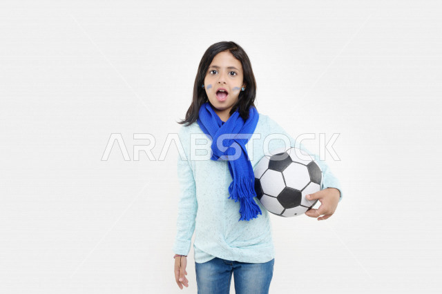 بورتريه لفتاة عربية خليجية سعودية مبتسمة مشجعة لفريق الهلال لكرة القدم السعودي ، تمسك بيدها كرة القدم بإيماءات تدل على الدهشة ، مشجعة لكرة القدم السعودي ، خلفية بيضاء