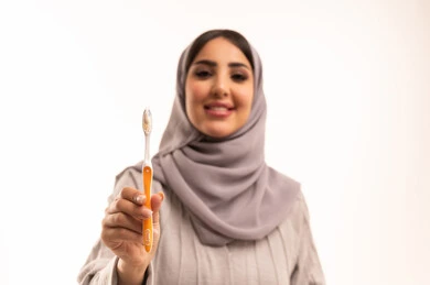 Maintaining and continuously cleaning teeth, the concept of healthy habits, a bright white smile, daily oral hygiene routine, avoiding cavities and gum diseases, a close-up portrait of a Saudi Gulf Arab woman wearing a hijab and abaya holding a toothbrush in her hands, white background.
