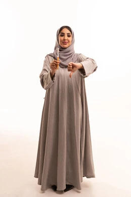 روتين نظافة الفم اليومية، الإشارة بعلامة عدم القبول والجودة السيئة، مفهوم العناية والاهتمام بصحة ونظافة الأسنان، بورتريه لامرأة عربية خليجية سعودية ترتدي الحجاب و العباءة تقوم بيديها فرشاة اسنان، الجسم بالطول الكامل، خلفية بيضاء