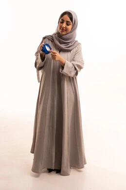 تحسين مظهر الجلد من خلال الترطيب والتنظيف، استخدام مكونات تجميلية شبابية، بورتريه لامرأة عربية خليجية سعودية ترتدي الحجاب و العباءة تضع كريم المرطب على يديها، الجسم بالطول الكامل، خلفية بيضاء