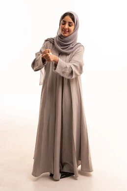 Using youthful cosmetic ingredients, the concept of caring for skin freshness and improvement, moisturizing, cleansing, and brightening the skin, skincare routine, a portrait of a Saudi Gulf Arab woman wearing a hijab and abaya applying moisturizer to her hands, full-body, white background.