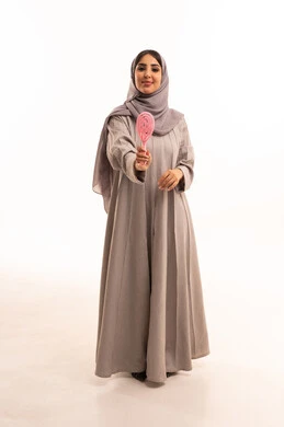 المحافظة على شعر صحي وأنيق، ترتيب وتمشيط الشعر، مفهوم العناية والاهتمام بالجمال والأناقة والمظهر الخارجي،بورتريه لامرأة عربية خليجية سعودية ترتدي الحجاب و العباءة تمسك بيدها فرشاة الشعر ( المشط ) بتعابير وإيماءات تدل على السعادة والسرور، الجسم بالطول الكامل، خلفية بيضاء