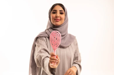 ترتيب وتمشيط الشعر، المحافظة على شعر صحي وأنيق، مفهوم العناية والاهتمام بالجمال والأناقة والمظهر الخارجي، بورتريه مقرب لامرأة عربية خليجية سعودية ترتدي الحجاب و العباءة تمسك بيدها فرشاة الشعر ( المشط ) بتعابير وإيماءات تدل على السعادة والسرور، خلفية بيضاء