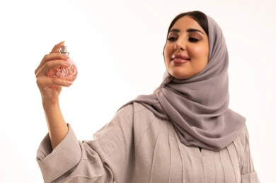 مفهوم الأناقة والإهتمام بالمظهر الخارجي، التطيب والتعطر بالعود والزيوت العطرية, بورتريه مقرب لامرأة عربية خليجية سعودية ترتدي الحجاب و العباءة تقوم برش العطر, التسويق لمنتجات العطور والمستحضرات النسائية، خلفية بيضاء
