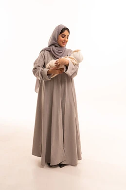 قضاء أوقات ممتعه مع الأطفال، الرعايه والاهتمام بالابناء, بورتريه لإمرأة عربيه خليجيه سعوديه ترتدي العباءة و الحجاب تحمل طفلتها بحب وحنان، تعابير السعادة و السرور، الجسم بالطول الكامل، خلفية بيضاء