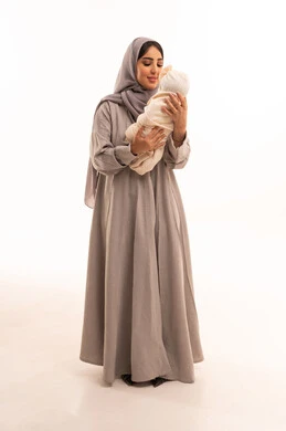 The tenderness of mothers, the responsibility and care for children, gestures of love and affection towards the little ones, a portrait of an Arab Gulf Saudi woman wearing an abaya and hijab, holding her daughter with love and tenderness, full-body, white background.