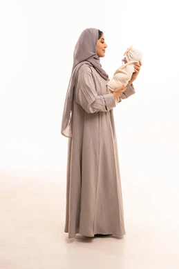 The importance of the mother and her essential role in raising and nurturing children, a side portrait of an Arab Gulf Saudi woman wearing an abaya and hijab, holding her daughter with love and tenderness, full-body, white background.