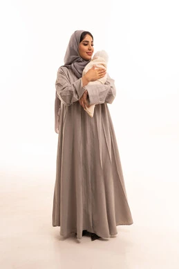 مفهوم الأمومه والطفولة، شعور الطفلة بالراحه والهدوء برفقه والدتها, ورترية لامراه عربيه خليجيه سعودية ترتدي العباءة و الحجاب تحمل ابنتها بلطف, اهتمام الأمهات بأبنائهم, دور الأم في تربيه وتنشأه الأولاد, الجسم بالطول الكامل، خلفيه بيضاء