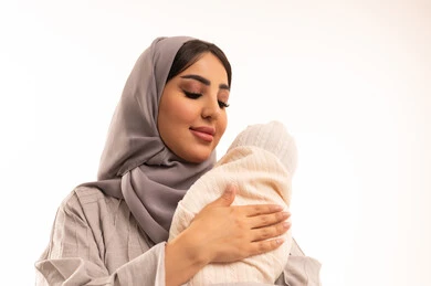 The role of the mother in raising and nurturing children, the feeling of comfort and tranquility of the little girl in the company of her mother, a close portrait of an Arab Gulf Saudi woman wearing an abaya and hijab gently holding her daughter, the care of mothers for their children, the concept of motherhood and childhood, white background.