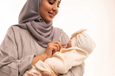 اللعب مع الأطفال بإيماءات السرور والسعاده,بورترية مقرب لامراه عربيه خليجيه سعودية ترتدي العباءة و الحجاب تداعب طفلتها, أهميه قضاء وقت ممتع مع حديثي الولاده, دور الأم في حياه الأبناء, مشاعر الحب والحنان بين الأم وأولادها, خلفيه بيضاء