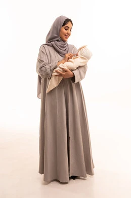 مشاعر الحب والحنان بين الأم وأولادها، اللعب مع الأطفال بإيماءات السرور والسعاده, بورترية لامراه عربيه خليجيه سعودية ترتدي العباءة و الحجاب تداعب طفلتها, أهميه قضاء وقت ممتع مع حديثي الولاده, دور الأم في حياه الأبناء, الجسم بالطول الكامل، خلفيه بيضاء