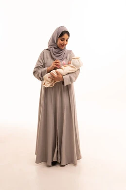 مفهوم الأمومة والرضاعة الصناعية، بورترية لامراه عربيه خليجيه سعودية ترتدي العباءة و الحجاب تقوم بإعطاء طفتلها الحليب من عبوة الرضاعة، الرعايه والاهتمام بتغذية ونمو الأبناء, قضاء أوقات ممتعه مع الأطفال, الجسم بالطول الكامل، خلفية بيضاء