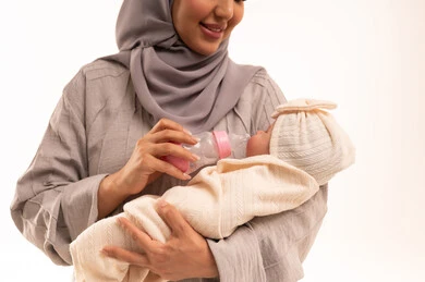 الرعايه والاهتمام بتغذية ونمو الأبناء، مفهوم الأمومة والرضاعة الصناعية، بورترية مقرب لامراه عربيه خليجيه سعودية ترتدي العباءة و الحجاب تقوم بإعطاء طفلتها الحليب من عبوة الرضاعة, قضاء أوقات ممتعه مع الأطفال, خلفية بيضاء