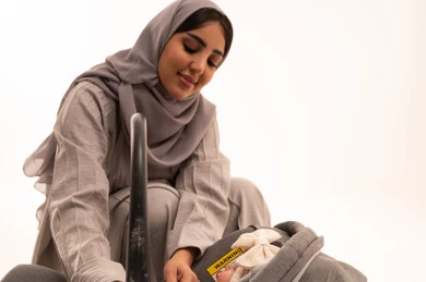 The interest of mothers in their children and their care, feelings of tenderness and affection, a close portrait of a Gulf Arab Saudi woman wearing an abaya and hijab looking at her infant daughter with gestures of happiness and love, white background.