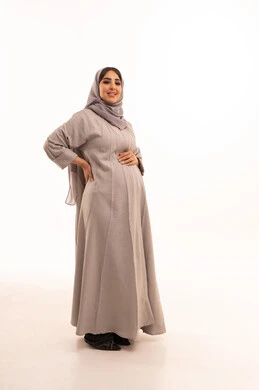 النظر للكاميرا بايماءات السعادة و السرور، مفهوم الحمل والانجاب، بورترية لامراه عربيه خليجيه سعودية حامل تضع يدها على بطنها تنتظر قدوم مولودها، الاهتمام بصحة الجنين، الجسم بالطول الكامل، خلفية بيضاء