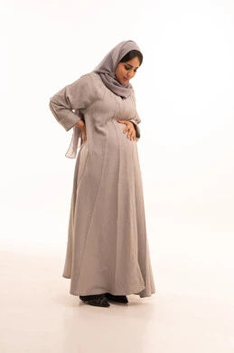 تعابير الألم ووجع الظهر، الشعور بالمرض والإرهاق، الحاجة للعلاج والاستشارة الطبية، بورترية لامراه عربيه خليجيه سعودية حامل ترتدي العباءة و الحجاب تضع يدها على ظهرها بايماءات التعب، صورة لكامل الجسم، خلفية بيضاء