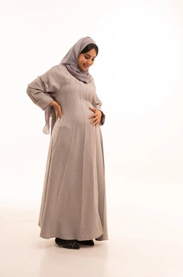 الحفاظ على صحتها و صحة طفلها، الاهتمام بصحة الجنين، مفهوم الحمل والانجاب، بورترية لامراه عربيه خليجيه سعودية حامل ترتدي العباءة و الحجاب تنظر إلى بطنها بإيماءات الحماس، الجسم بالطول الكامل، خلفية بيضاء