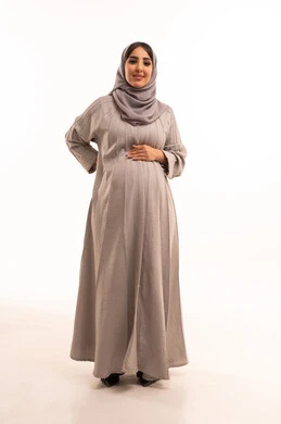 الشعور بالمرض والإرهاق، الحاجة للعلاج والاستشارة الطبية، تعابير الألم ووجع الظهر، بورترية لامراه عربيه خليجيه سعودية حامل ترتدي العباءة و الحجاب تضع يدها على ظهرها بايماءات التعب، صورة لكامل الجسم، خلفية بيضاء